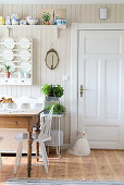 Rustic table in front of plate rack in kitchen-dining room with white door and wood-clad wall