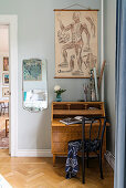 Antique bureau in corner of room below anatomical drawing decorating wall