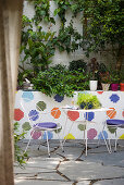 Filigraner Metalltisch und zwei Stühle auf Terrasse mit bunten Mosaik-Wandfliesen