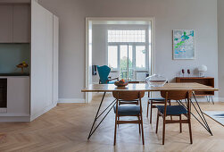 Dining table with slender lines and chairs in open-plan interior with kitchen in custom-made cube