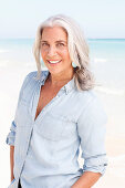 A mature woman with white hair on a beach wearing a light blue blouse
