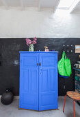 Blue half-height cabinet, shopping bags hung from wall hooks and black vase on floor against wall painted black and white