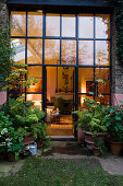 View into warmly lit interior through glass wall with lattice frame at twilight