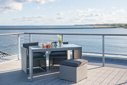 Graue Outdoormöbel auf offen gehaltener Terrasse mit Holzplankenboden und Meerblick