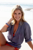 A blonde woman on a beach wearing a red bikini and a blue blouse