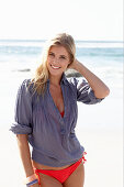 A blonde woman on a beach wearing a red bikini and a blue blouse