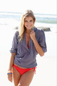Blonde Frau in rotem Bikini und blauer Bluse am Strand