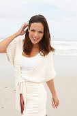 A brunette woman by the sea wearing a short-sleeved cardigan