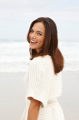 A brunette woman by the sea wearing a short-sleeved cardigan