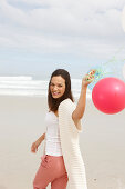 Brünette Frau mit Luftballon in Strickjacke mit kurzen Ärmeln am Meer