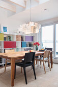 Designer lamp above dining table in front of shelving with colourful compartment doors