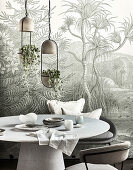 Round table with chairs above, pendant lights with house plants in front of wallpaper with jungle motif
