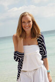 Junge Frau in weißem Sommerkleid und gestreiftem Jäckchen am Strand