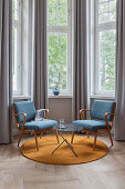 Blaue Sessel und Beistelltisch auf rundem, senfgelbem Teppich im Erker