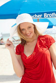 A blonde woman on a beach wearing a red top and a white hat