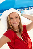 A blonde woman on a beach wearing a red top and a white hat