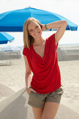 A blonde woman on a beach wearing a red top and shorts