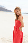 A young blonde woman on a beach wearing a red summer dress