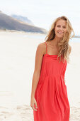 A young blonde woman on a beach wearing a red summer dress