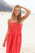 A young blonde woman on a beach wearing a red summer dress