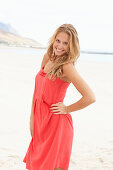 A young blonde woman on a beach wearing a red summer dress