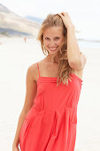 A young blonde woman on a beach wearing a red summer dress