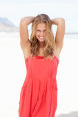 A young blonde woman on a beach wearing a red summer dress