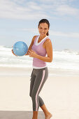 A young brunette woman by the sea wearing sports clothes with a ball