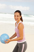 A young brunette woman by the sea wearing sports clothes with a ball