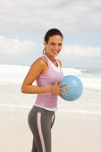 A young brunette woman by the sea wearing sports clothes with a ball