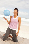 A young brunette woman by the sea wearing sports clothes with a ball