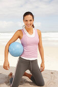 A young brunette woman by the sea wearing sports clothes with a ball