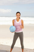 A young brunette woman by the sea wearing sports clothes with a ball