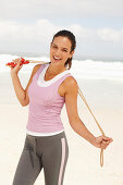 A young brunette woman by the sea wearing sports clothes with a skipping rope