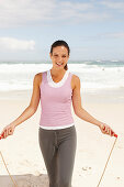 A young brunette woman by the sea wearing sports clothes with a skipping rope