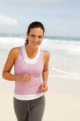 A young brunette woman jogging by the sea wearing sports clothes