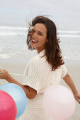 A brunette woman wearing a short-sleeved cardigan and holding balloons