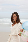 A brunette woman wearing a short-sleeved cardigan and holding balloons