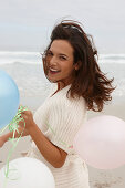 A brunette woman wearing a short-sleeved cardigan and holding a balloon