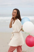 A brunette woman wearing a short-sleeved cardigan and holding a balloon