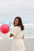 A brunette woman wearing a short-sleeved cardigan and holding a balloon