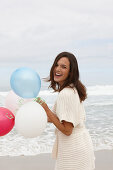 A brunette woman wearing a short-sleeved cardigan and holding a balloon