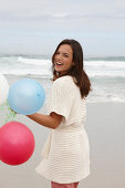 A brunette woman wearing a short-sleeved cardigan and holding a balloon