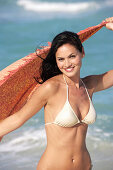 A young brunette woman on a beach with a towel wearing a silver bikini