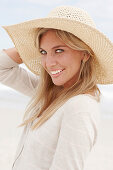 A blond woman on a beach wearing a light cardigan and a summer hat