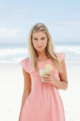 A young woman on a beach with a smoothie wearing a pink top