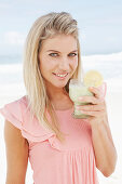 A young woman on a beach with a smoothie wearing a pink top