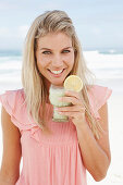 A young woman on a beach with a smoothie wearing a pink top