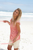 A young woman on a beach with a hula-hoop wearing a pink top and shorts