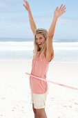 A young woman on a beach with a hula-hoop wearing a pink top and shorts